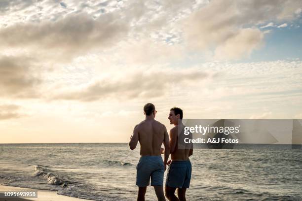 jeune couple homosexuel marchant sur la plage - gay men swimwear photos et images de collection