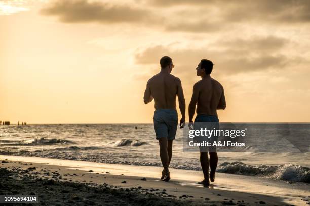 young homosexual couple walking on the beach - gay cuba stock pictures, royalty-free photos & images