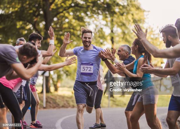 allegro maratoneta che saluta gruppo di atleti al traguardo. - gara sportiva foto e immagini stock