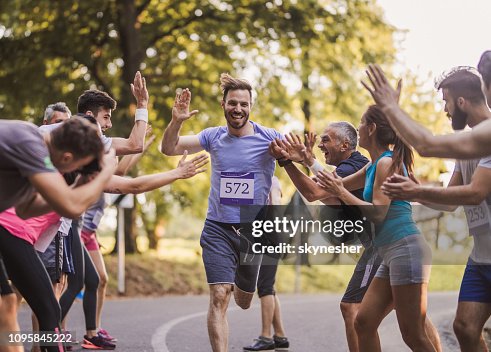 Cheerful marathon runner greeting group of athletes at finish line. Cheerful marathon runner greeting group of athletes at finish line.