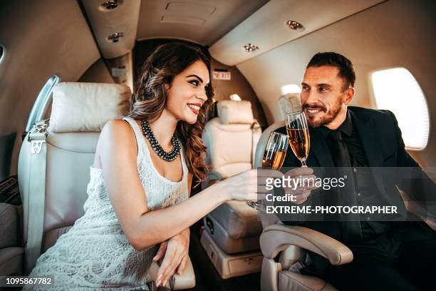 junge reiche paar machen einen toast beim sitzen nebeneinander auf einem privaten flugzeug - millionnaire stock-fotos und bilder