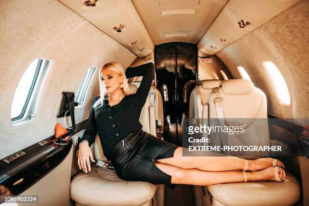 rich blond girl looking through window while sitting comfortably with feet up on a private jet - billionaire stock pictures, royalty-free photos & images