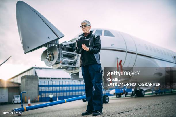 senior vrouwelijke ingenieur holding digitale tablet naast een een klein privé-vliegtuig met een geopende neus geparkeerd op een taxibaan - aviation worker stockfoto's en -beelden