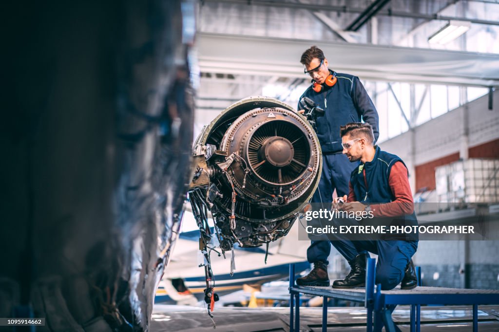 Dois técnicos trabalhando juntos em um motor de jato desmontado de um pequeno avião em um hangar de manutenção de aeronaves