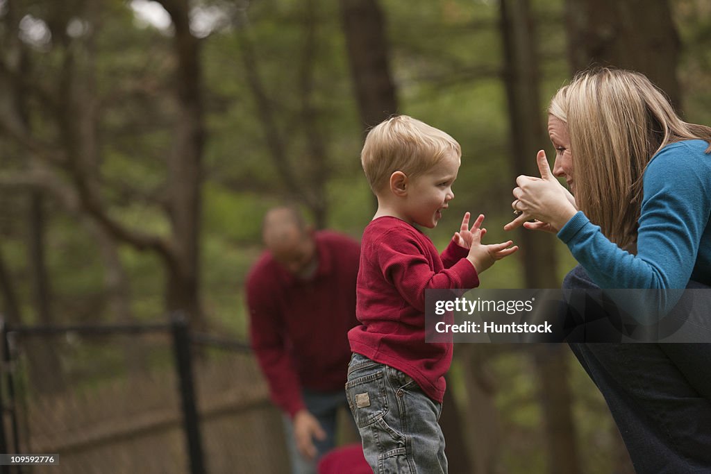 Woman signing the word 'Play' in American Sign Language while communicating with her son in a park