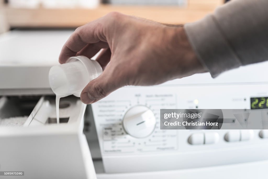 Man using dosing aid to fill fabric softener into washing machine