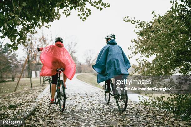 achteraanzicht van paar in regenjassen rijden een fietsen in het park - raincoat stockfoto's en -beelden