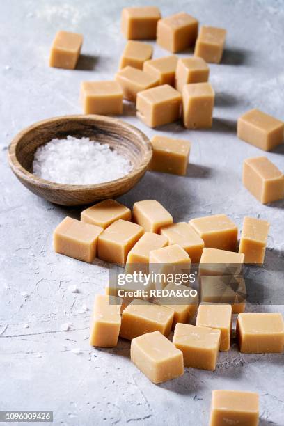 Salted caramel fudge candy served on wooden board with fleur de sel in wooden bowl over grey texture background Close up.