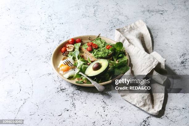 Vegetarian sandwiches with avocado, poached egg, spinach, cherry tomatoes on whole grain toast bread on ceramic plate with textile napkin over white...