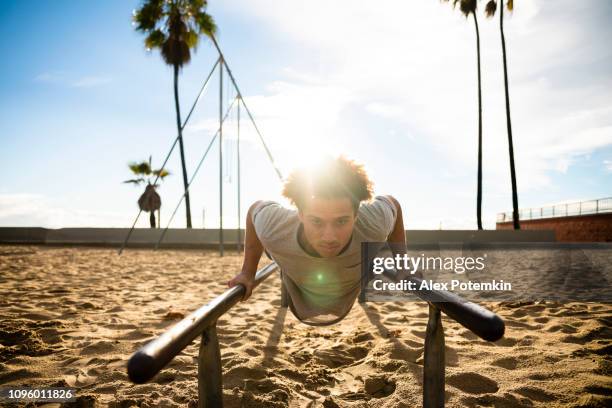 the young latino man doing push-up exercise on the bars - alex potemkin or krakozawr latino fitness stock pictures, royalty-free photos & images