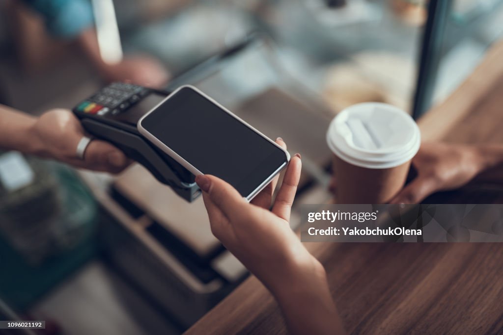Mano de joven colocando smartphone en máquina de pago de tarjeta de crédito