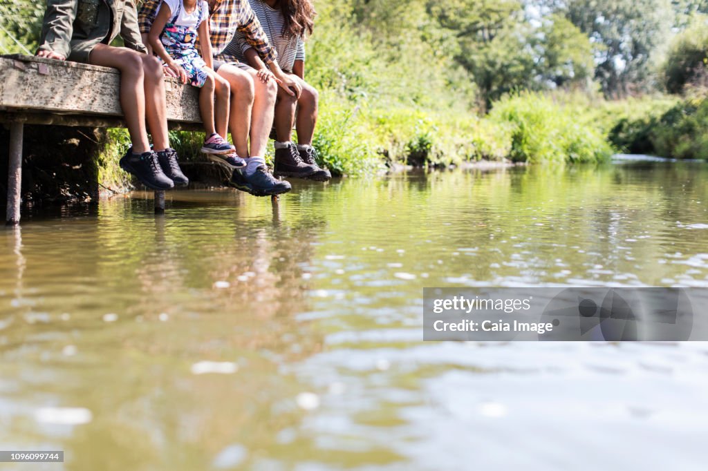 Family dangling feet off sunny riverside dock