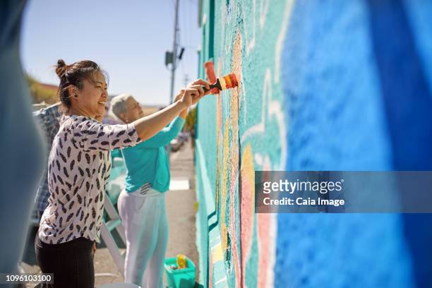 Women painting vibrant mural on sunny urban wall