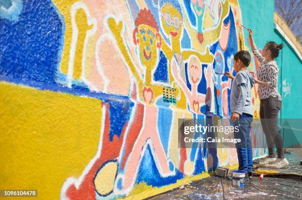 mother and son volunteers painting vibrant mural on sunny wall - mural wall stock pictures, royalty-free photos & images