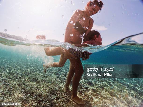 madre che insegna a sua figlia a nuotare - half underwater foto e immagini stock