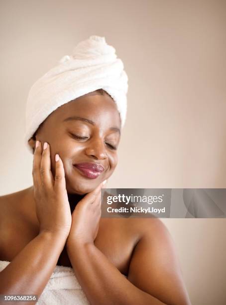 female at spa wrapped in towel touching her face skin. - african ethnicity spa stock pictures, royalty-free photos & images