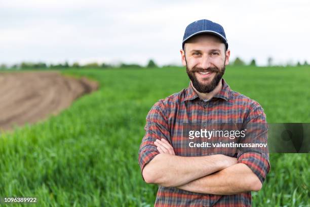 smiling farmer standing arms crossed in cultivated field - farmer arms crossed stock pictures, royalty-free photos & images