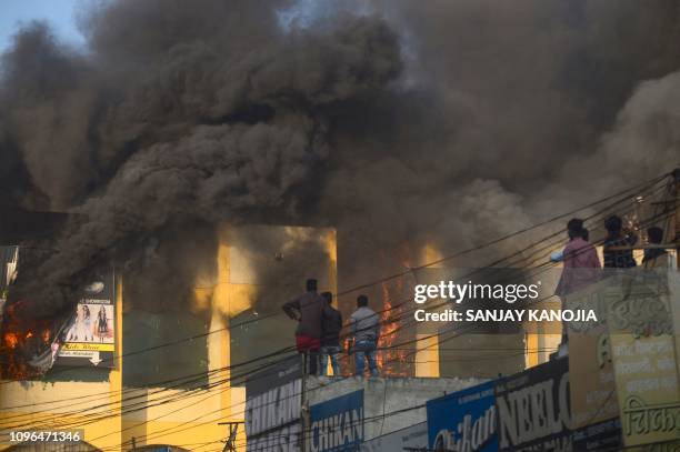 Indian people look on as smoke billows from the top floor after a fire broke out at a shopping complex in the old city in Allahabad on February 9,...
