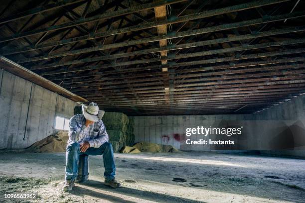 inside a barn, a desperate looking man sitting all by himself on a bucket. - concerned farmers stock pictures, royalty-free photos & images