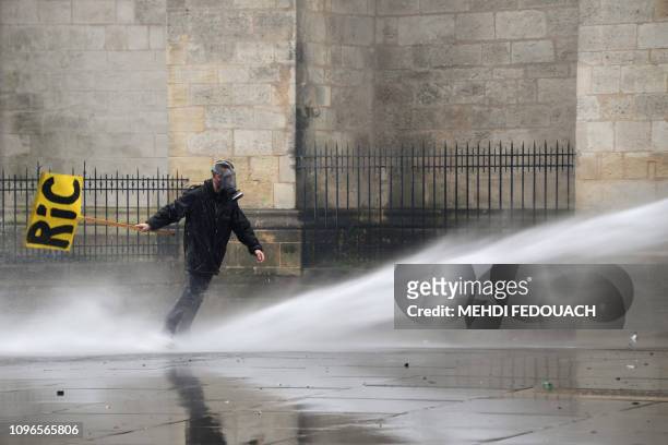 Man holding a placard reading RIC is seen as a riot police vehicle uses a water cannon to disperse protesters during a yellow vests rally, on...