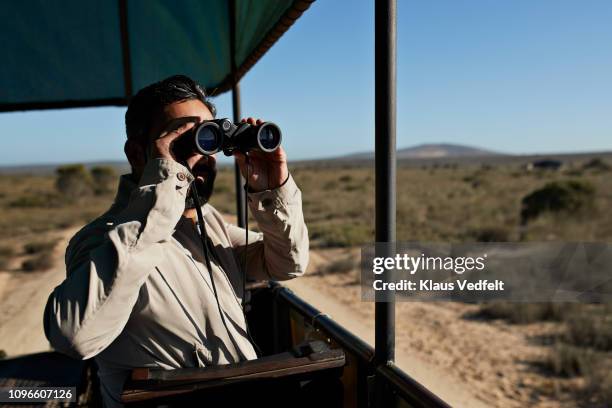 man watching wild animals threw binoculars from safari vehicle - man wearing cap photos et images de collection