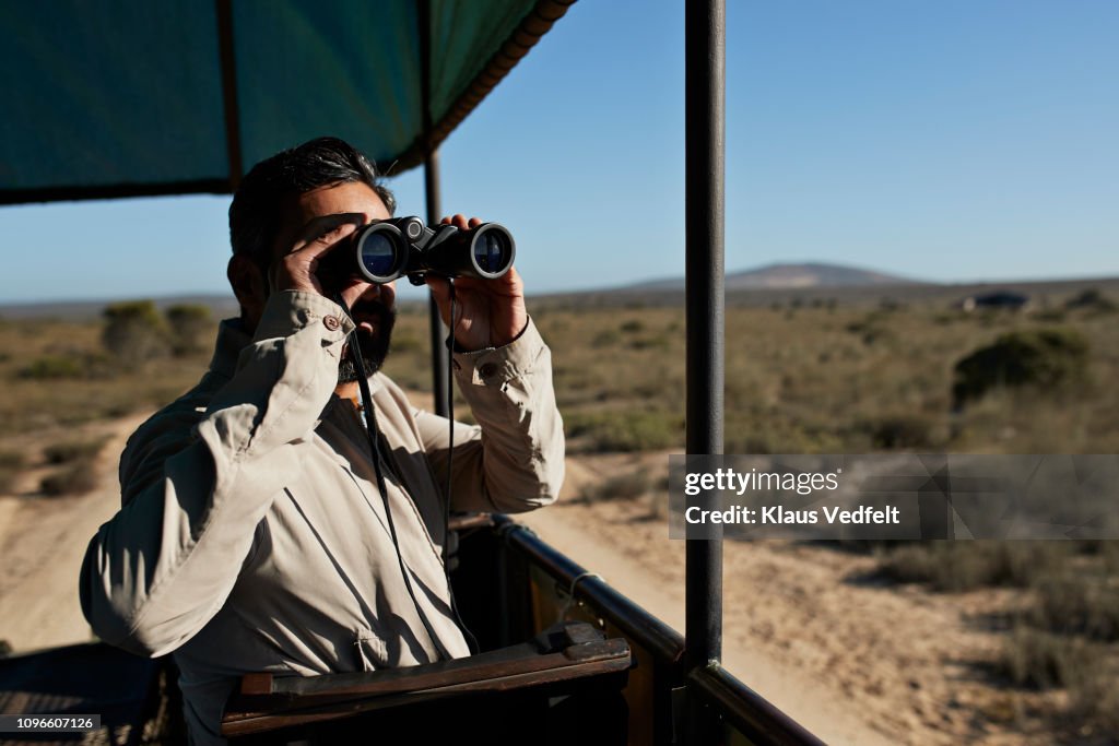 Man watching wild animals threw binoculars from safari vehicle