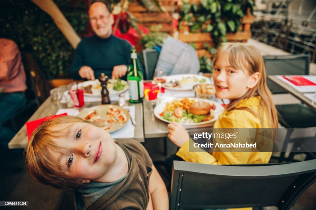 Happy family eating hamburger with french fries and pizza in outdoor restaurant