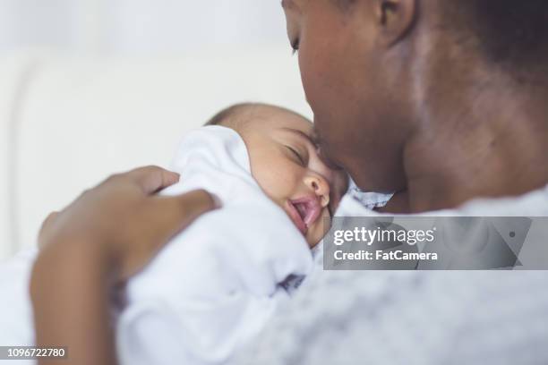 hermosa madre afroamericana en una bata de hospital tiene a su bebé recién nacido suavemente a su pecho - hospital gown fotografías e imágenes de stock