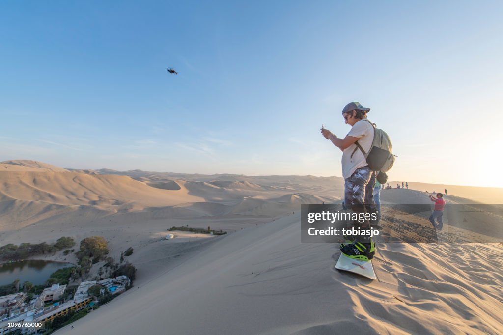 People sandboarding and flying drone in the desert