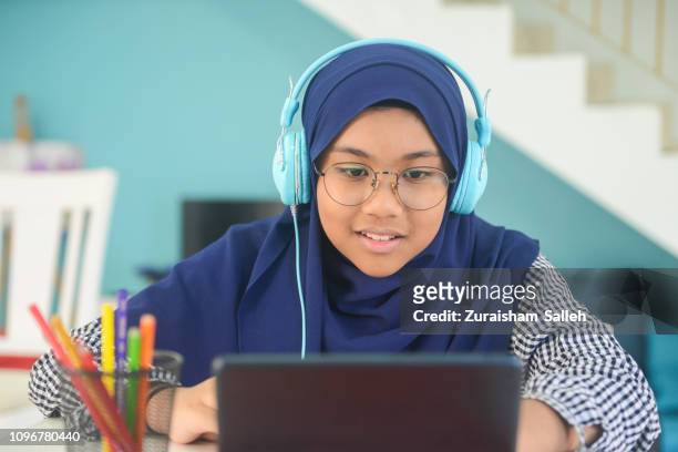 asian teenage girl with headphones doing homework with digital tablet - hijab student stock pictures, royalty-free photos & images