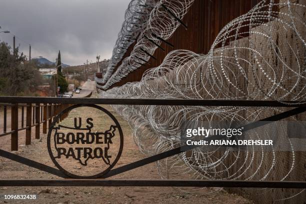 Metal fence marked with the US Border Patrol sign prevents people to get close to the barbed/concertina wire covering the US/Mexico border fence, in...