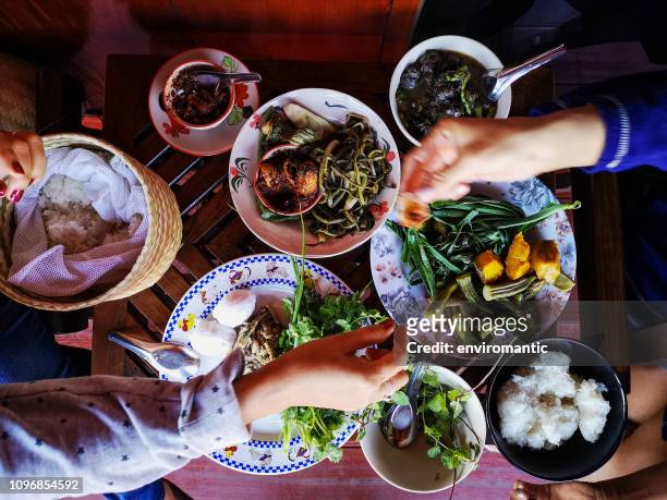 two thai women traditionally eating a selection of freshly cooked northern thai food of vegetables, soups and curries served in dishes on a wooden table, along with sticky rice, which is a food staple in northern and northeast thailand. - chiang mai province stock pictures, royalty-free photos & images