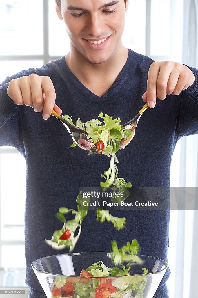 Young man mixing a bowl of fresh green salad