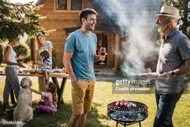 glückliche männer sprechen, während seine familie im hinterhof grill vorbereiten. - bbq father stock-fotos und bilder