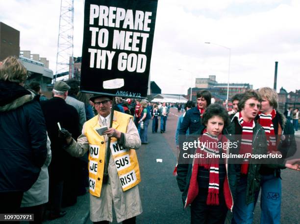 Manchester United supporters walk past an evangelist, who is carrying a placard with a biblical quotation from Amos, chapter 4, verse 12, 'Prepare to...