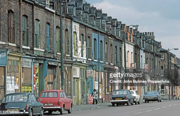 Cars parked on a street of boarded up shops, Manchester, England in 1976.