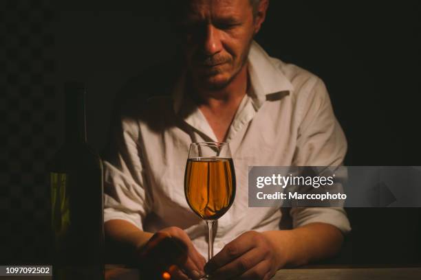 beautiful adult man with drinking problems holding glass of white wine in low light room - low alcohol drink stock pictures, royalty-free photos & images