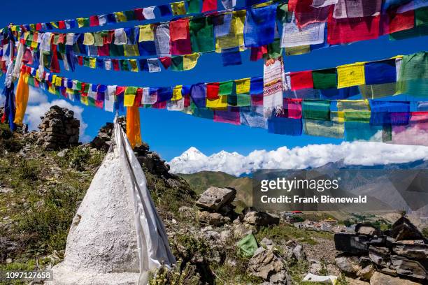Small chorten, stupas, are located above town, colorful buddhist prayer flags fluttering in the air, the snow covered summit of Mt. Dhaulagiri in the...