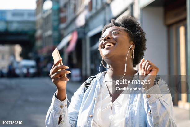 happy black woman listening to music with headphones on the street - streaming music stock pictures, royalty-free photos & images