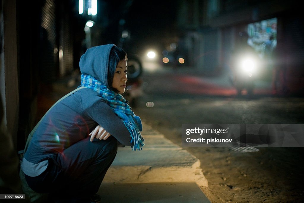 Asian woman sitting on street at night