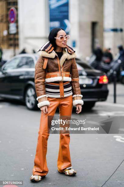Aleali May wears a brown leather aviator jacket, orange flare pants, black and white striped wool top, outside Acne, during Paris Fashion Week -...
