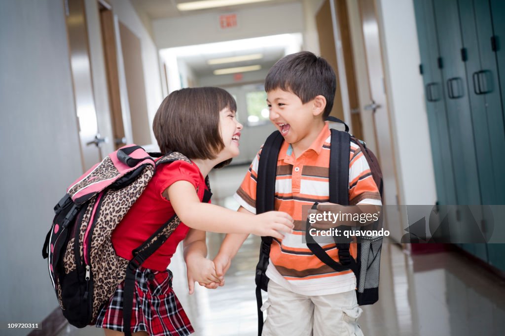 Süße Kinder mit Rucksäcken lachen in der Grundschule Korridor