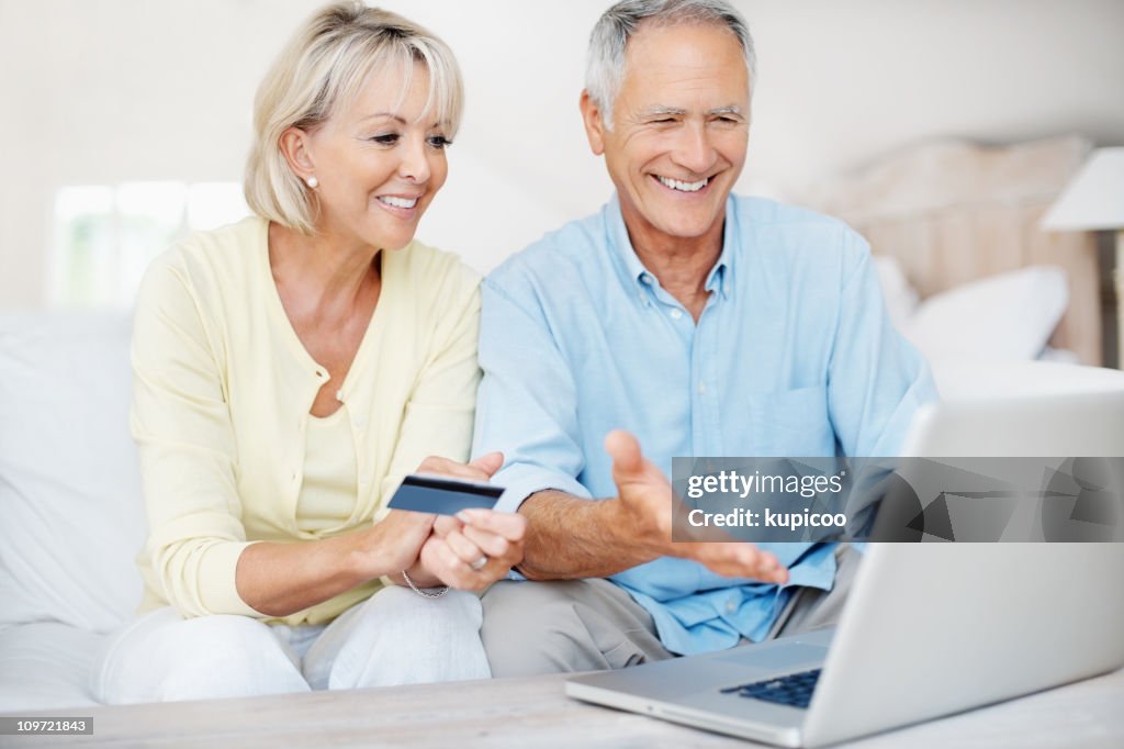 Happy mature couple using credit card to shop online