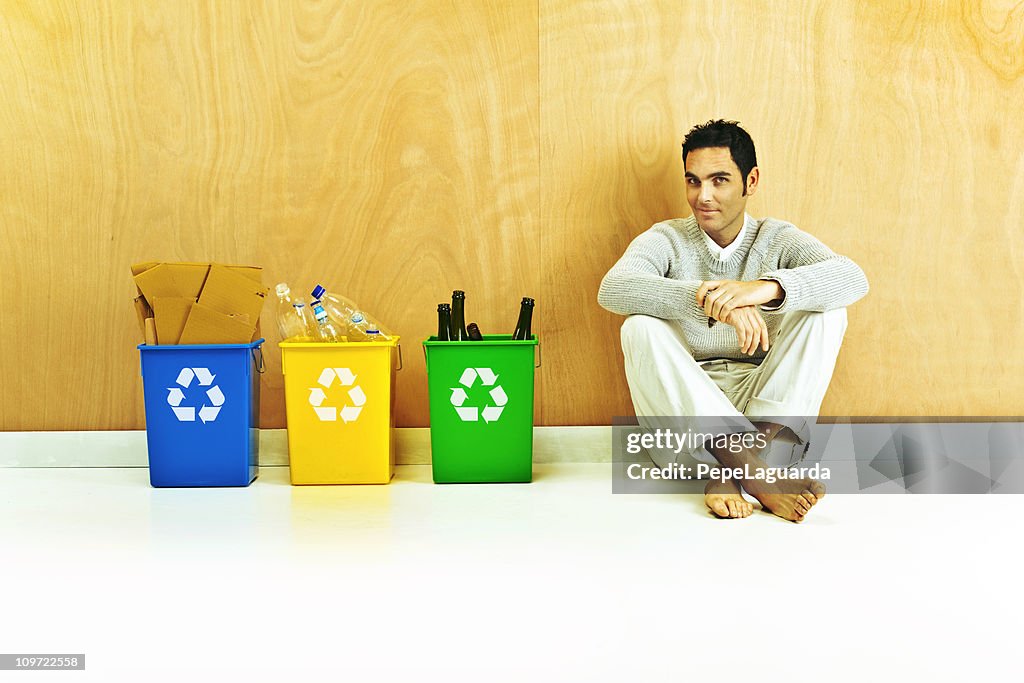 Homme assis par la présence de poubelles de recyclage