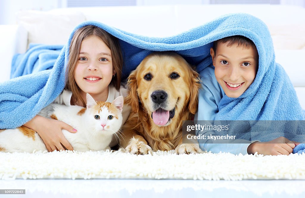 Children, dog and cat looking out the blanket.