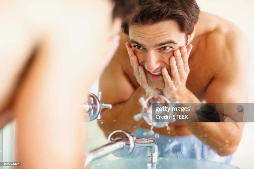 Happy young guy washing his face at the wash basin