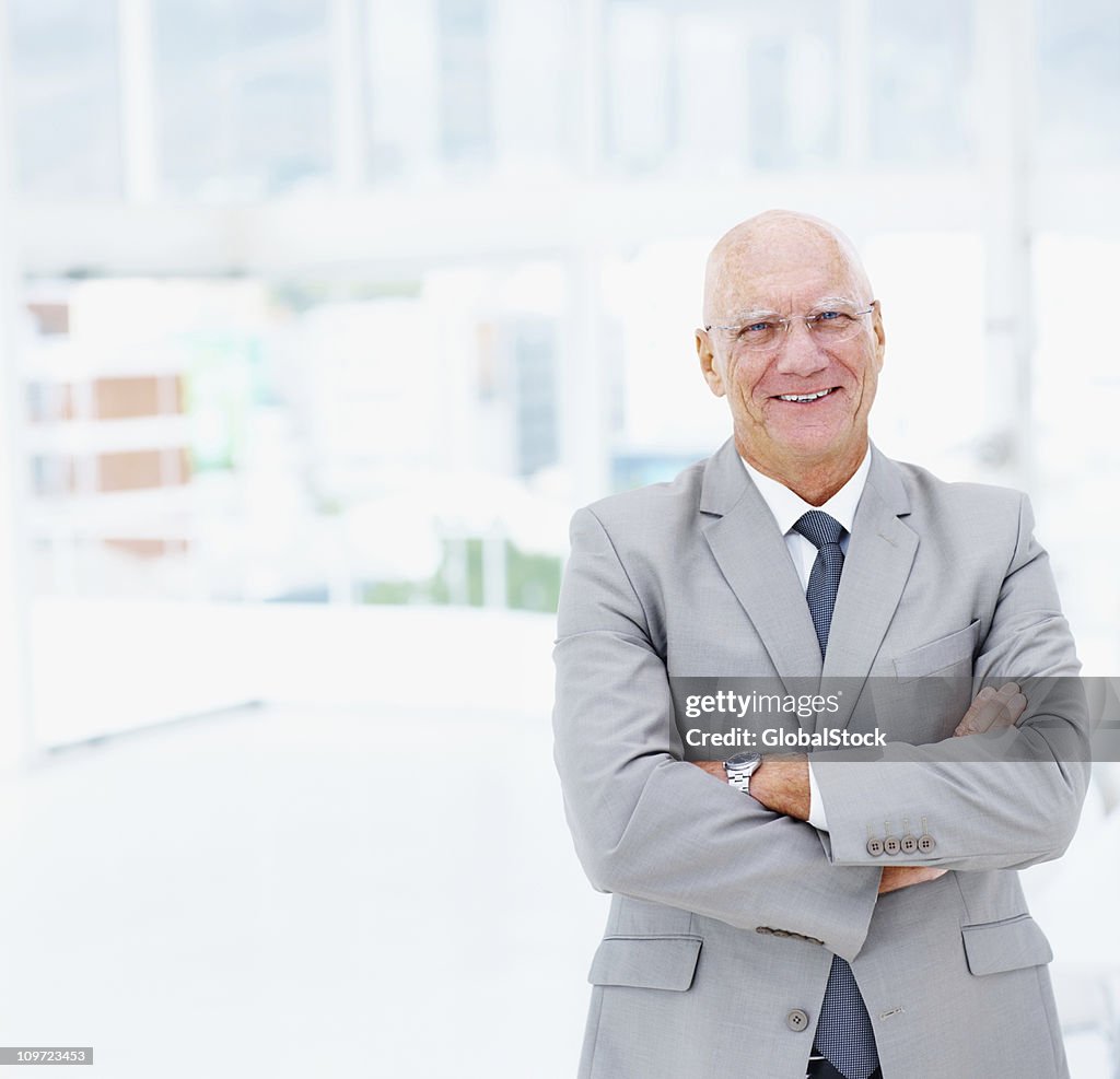 Senior business man with arms crossed smiling at office