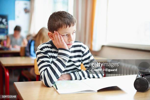 aborrecido pequeno menino de escola em sala de aula, olhando para fora da janela - distraído imagens e fotografias de stock