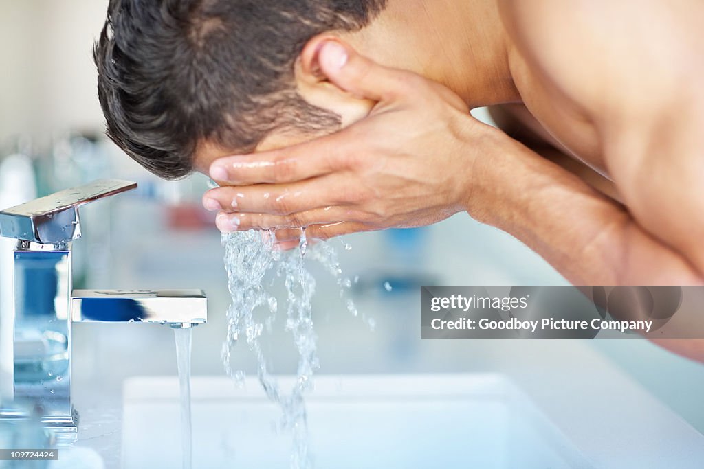 Young guy cleansing face with water at the sink