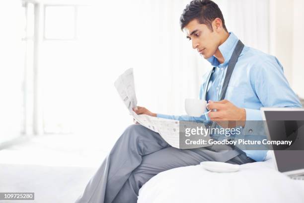 junge business mann, sitzend auf dem bett mit kaffee und tageszeitung - junger mann liest zeitung stock-fotos und bilder
